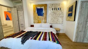 Un dormitorio con cama, una manta a rayas de colores y arte abstracto en la pared.
