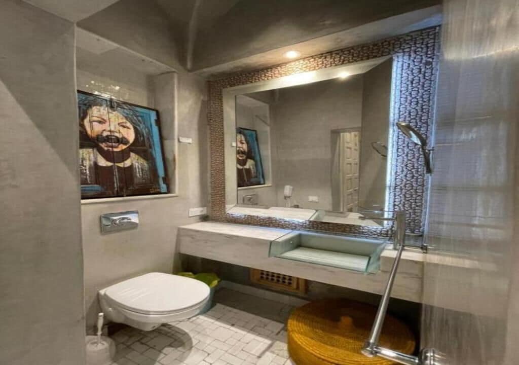 A bathroom with a modern design, featuring a toilet, sink, and mirror.