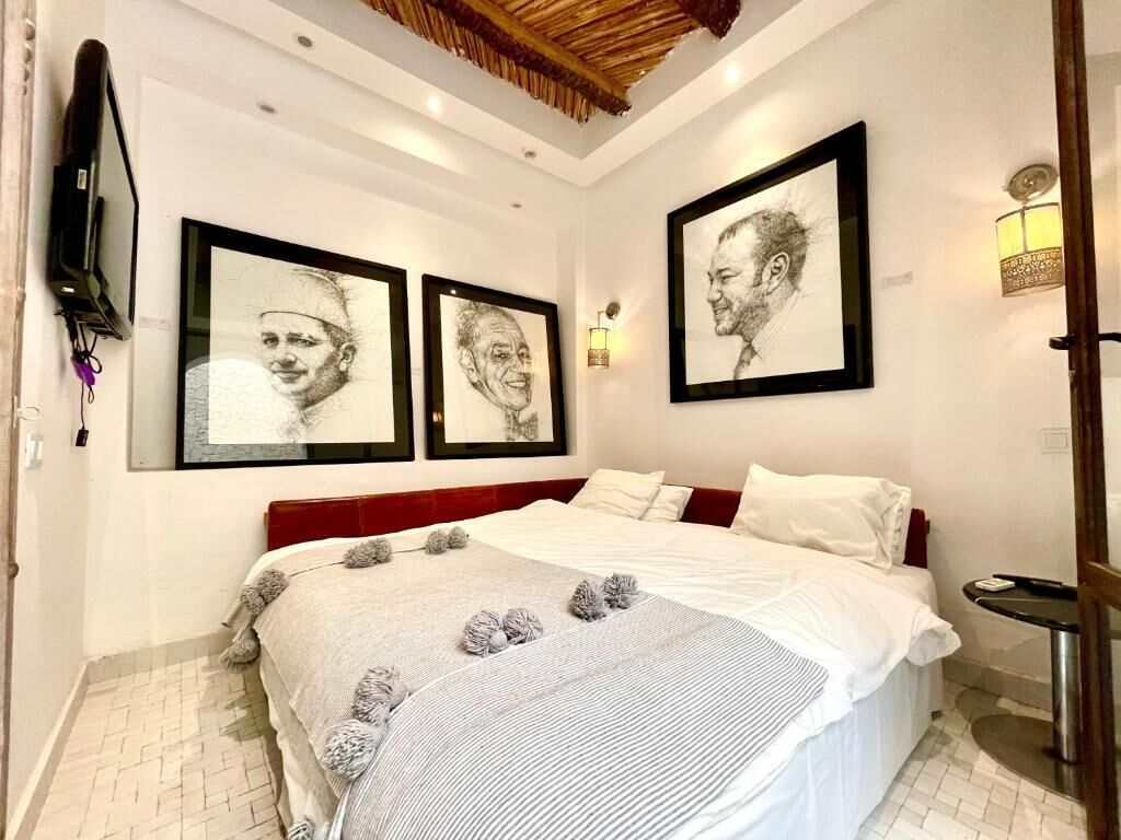 Un dormitorio con una cama, un televisor montado en la pared y cuadros colgados sobre la cama.