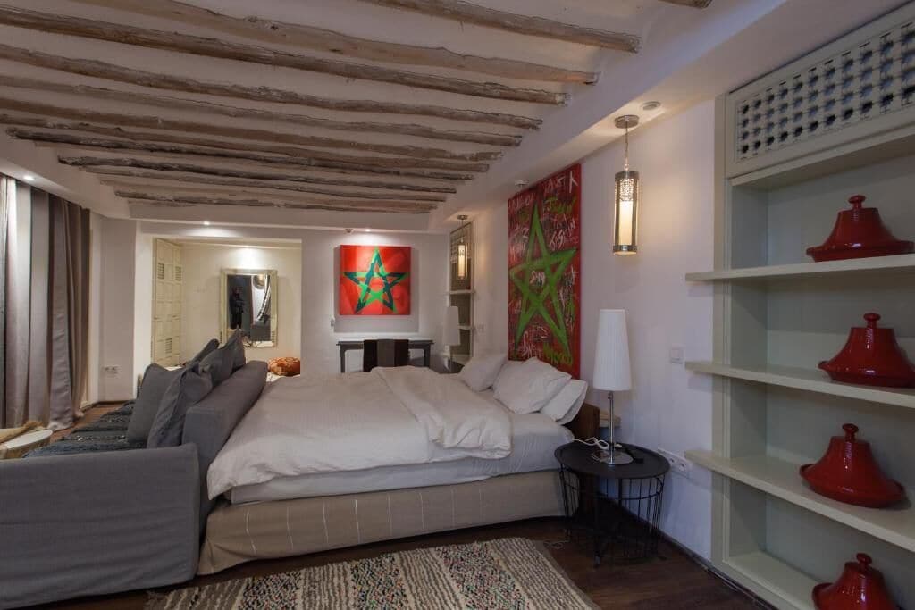 A bedroom with a bed, a bedside table, a lamp, and a wall with a geometric pattern.