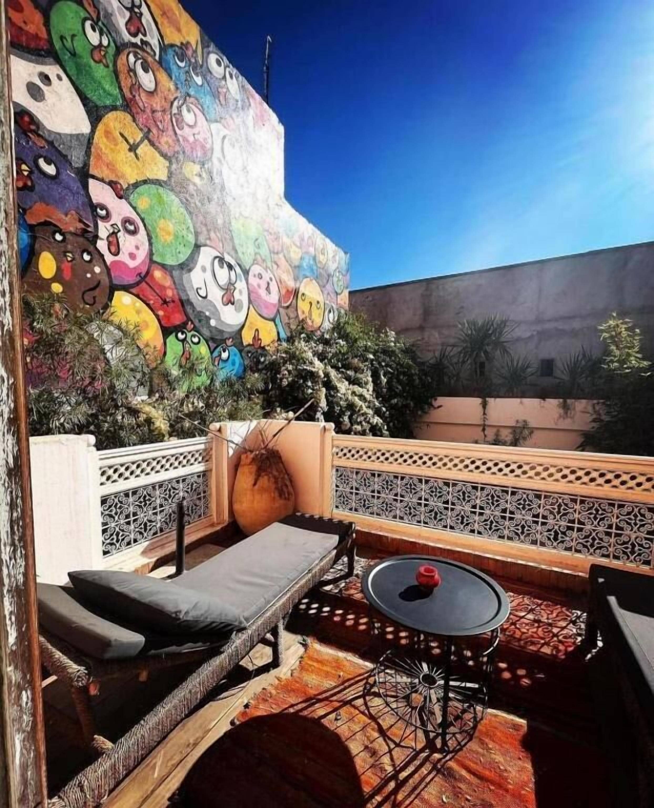 Eine Dachterrasse mit einer farbenfrohen Wandmalerei, Liegestühlen, einem kleinen Tisch und einem Zierzaun.