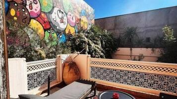 Eine Dachterrasse mit einer farbenfrohen Wandmalerei, Liegestühlen, einem kleinen Tisch und einem Zierzaun.