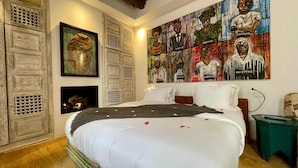 A bedroom with a large bed, a fireplace, and a wall with multiple artworks. - bck art riad (Marrakech)