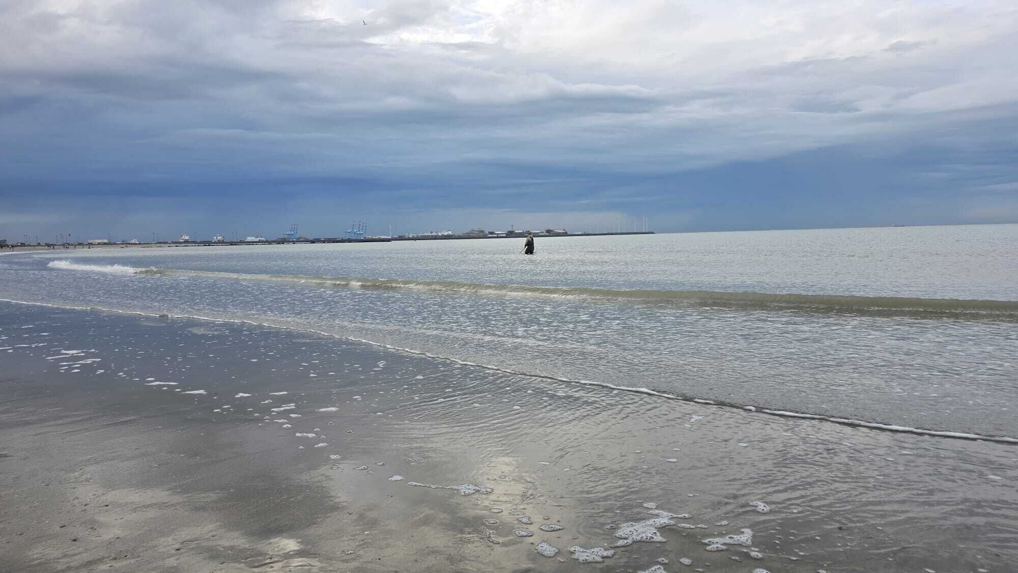 Une plage avec des vagues, une jetée au loin et un ciel nuageux.