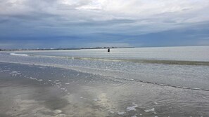 Ein Strand mit Wellen, ein weiter Pier und ein bewölkter Himmel.
