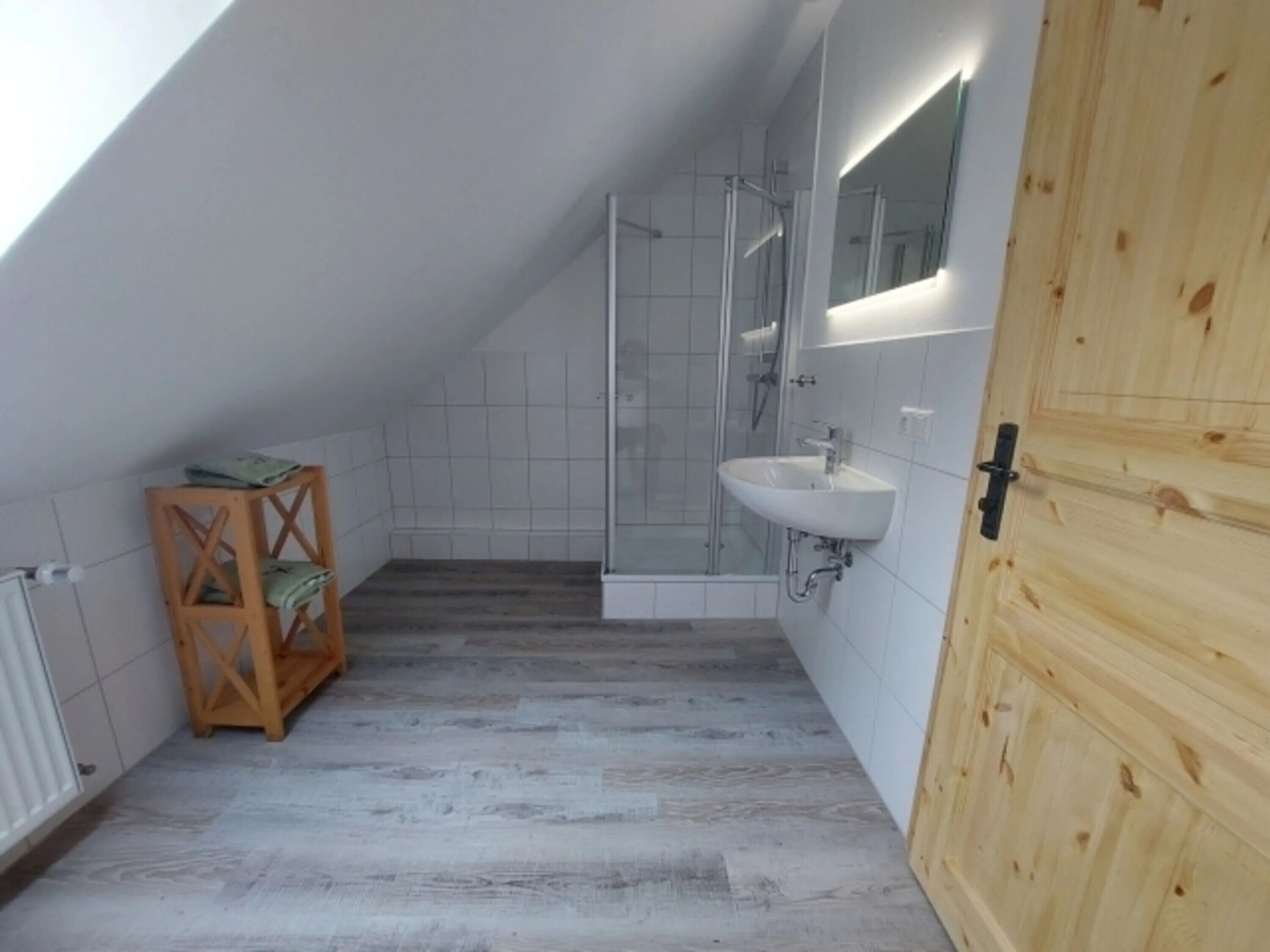 Een kleine badkamer met een douche, een wastafel en een houten plank.