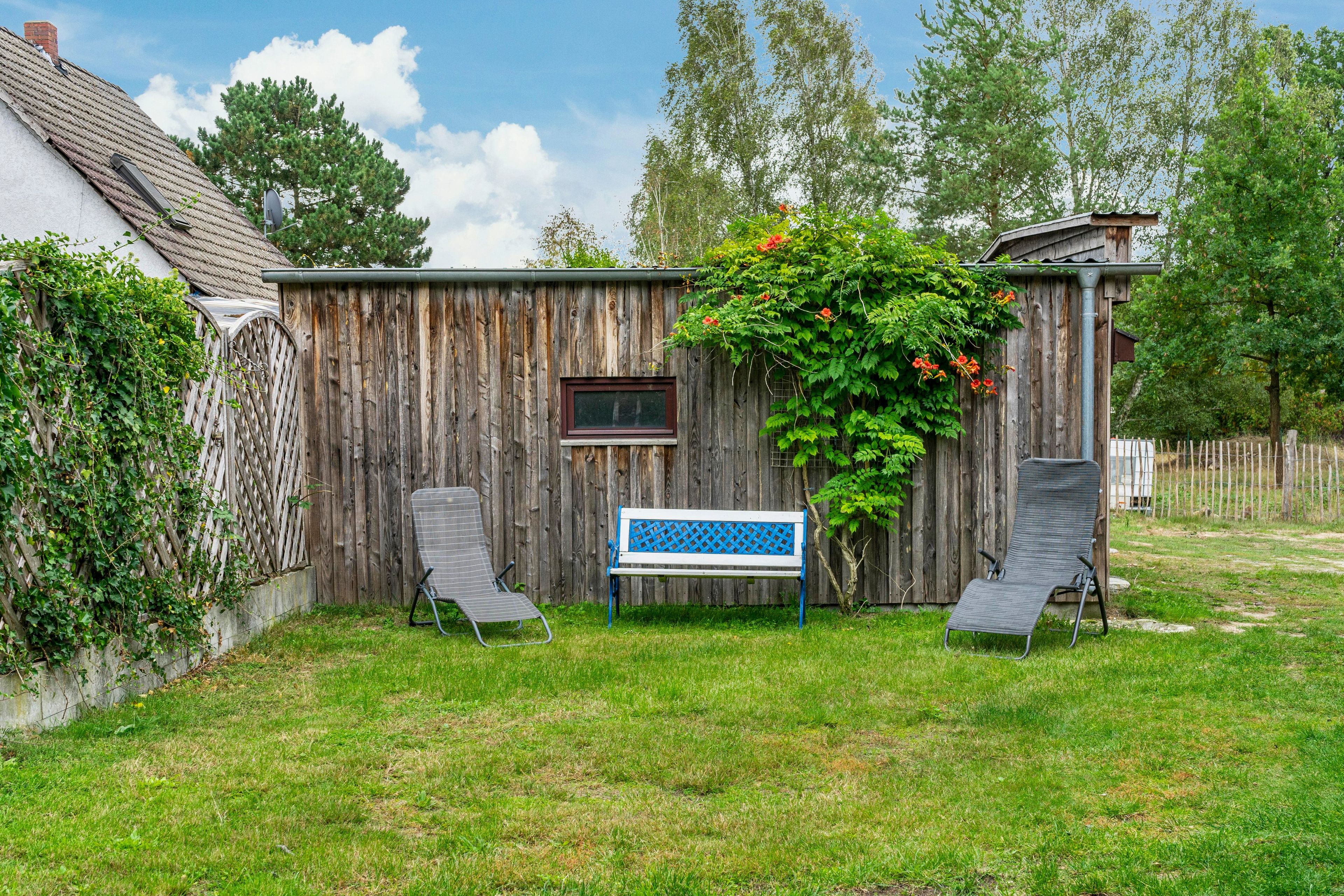 A wooden fence with a bench and two chairs in a backyard.