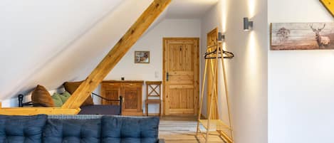 A room with a sloped ceiling, a sofa, a wooden cabinet, a door, and a wall-mounted light fixture.