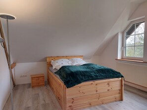 Un dormitorio con una cama de madera, una mesita de noche, una lámpara de pie y una ventana con vistas a árboles.