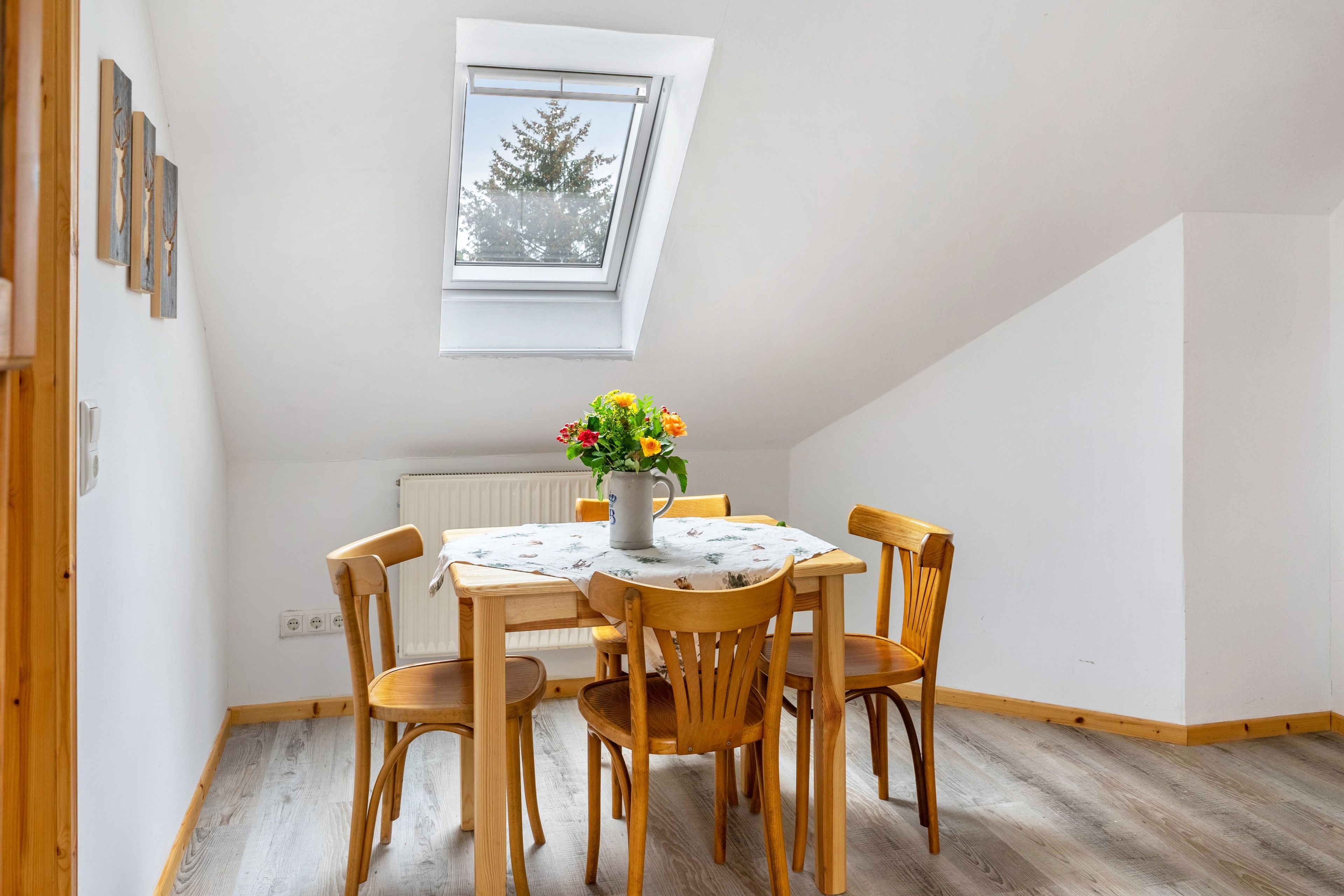 A dining area with a table and chairs, a window with a view of trees, and a radiator below.