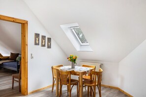 A dining area with a table and chairs, a skylight, and a bed in the background.