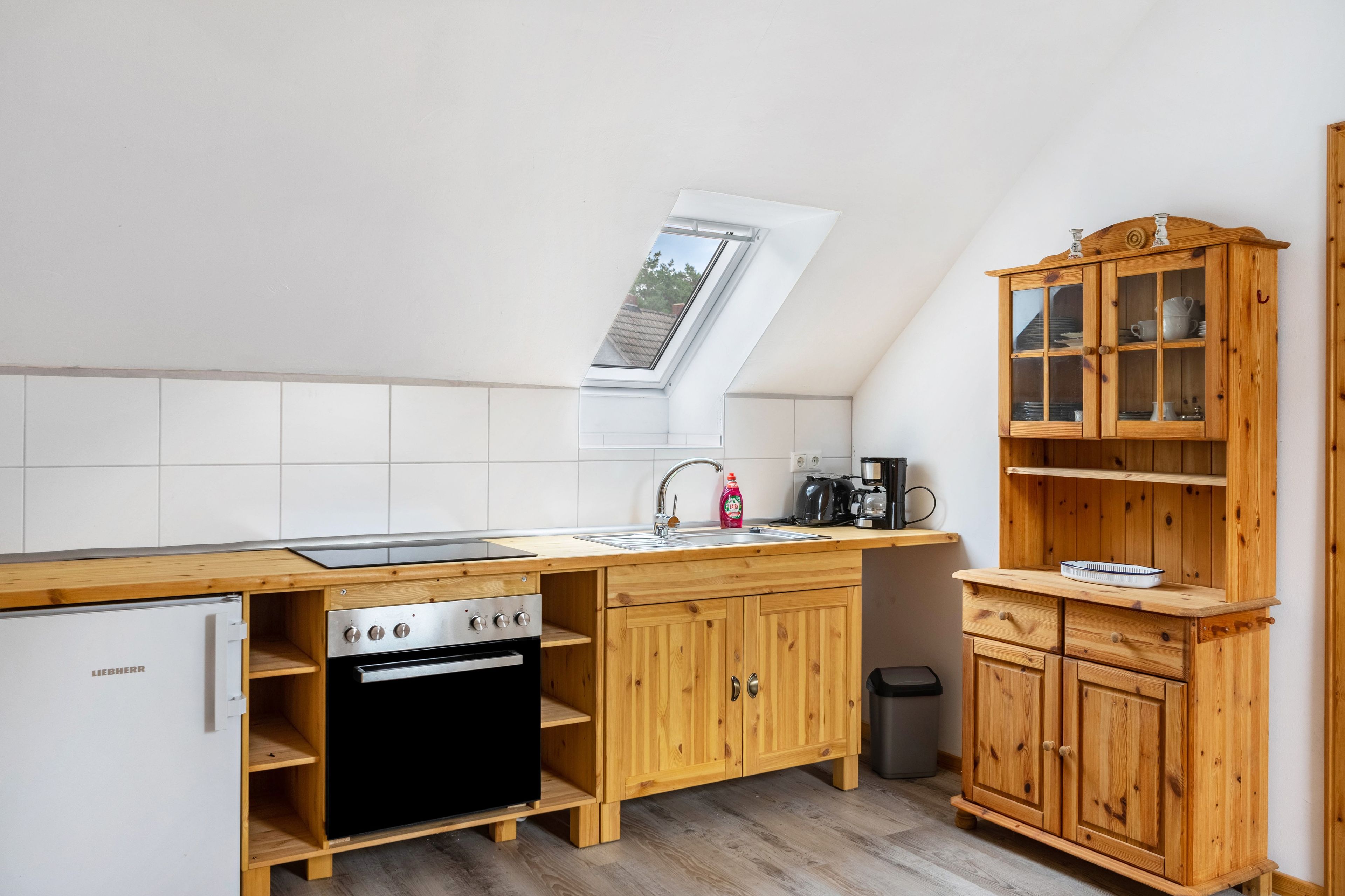 Una cocina compacta con horno integrado, un lavamanos y un mueble de madera con puertas de cristal.