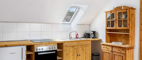 Une cuisine compacte équipée d’un four encastré, d’un évier et d’un meuble en bois doté de portes en verre.