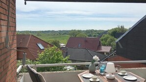 A balcony with a table set for two, overlooking a residential area with houses and greenery. - Apartment Vogelsang in Borkum (Borkum)