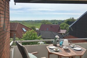 Ein Balkon mit Tisch für zwei Personen, mit Blick auf eine Wohngegend mit Häusern und Grünflächen.