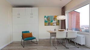 A compact living space with a dining area, a kitchenette, and a view of the cityscape. - Apartment Vogelsang in Borkum (Borkum)