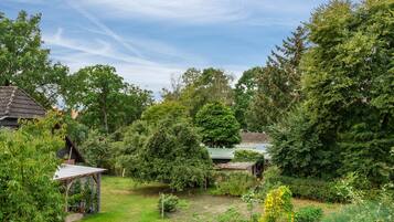 Ein Garten mit verschiedenen Bäumen und Sträuchern, einer kleinen Holzkonstruktion und blauem Himmel.
