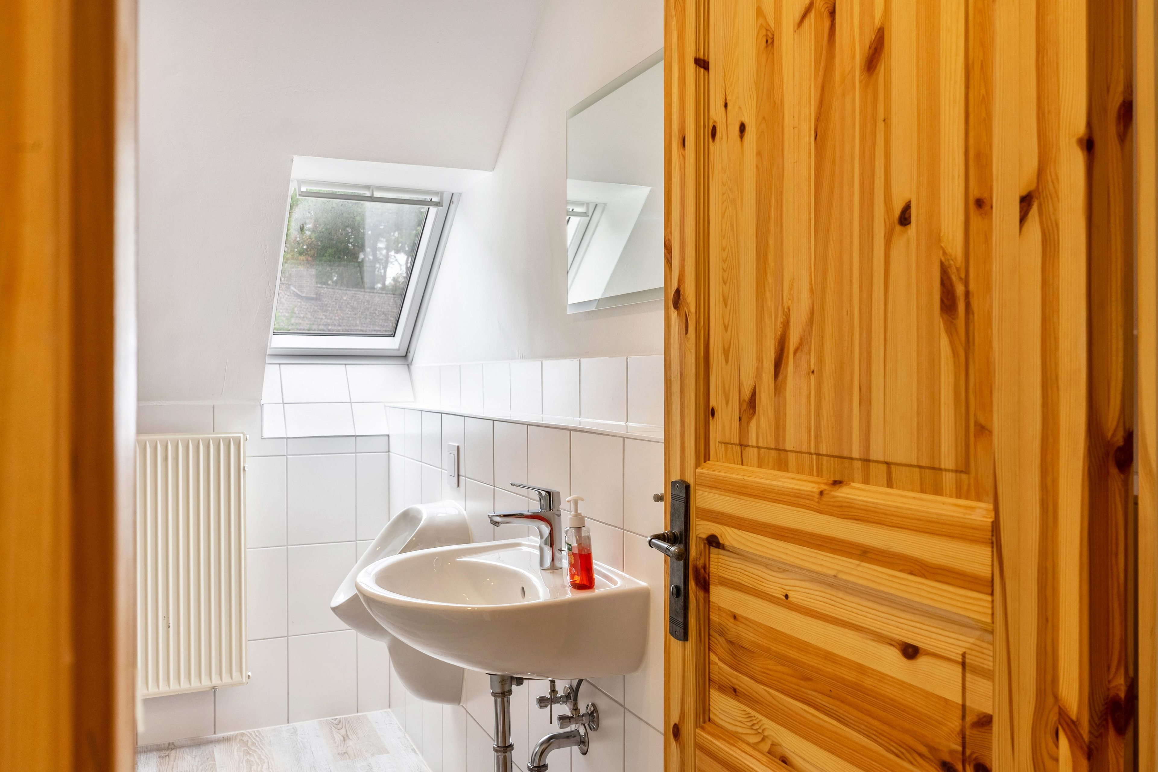 Ein modernes Badezimmer mit einem weißen Waschbecken, einem Spiegel und einem Oberlicht.