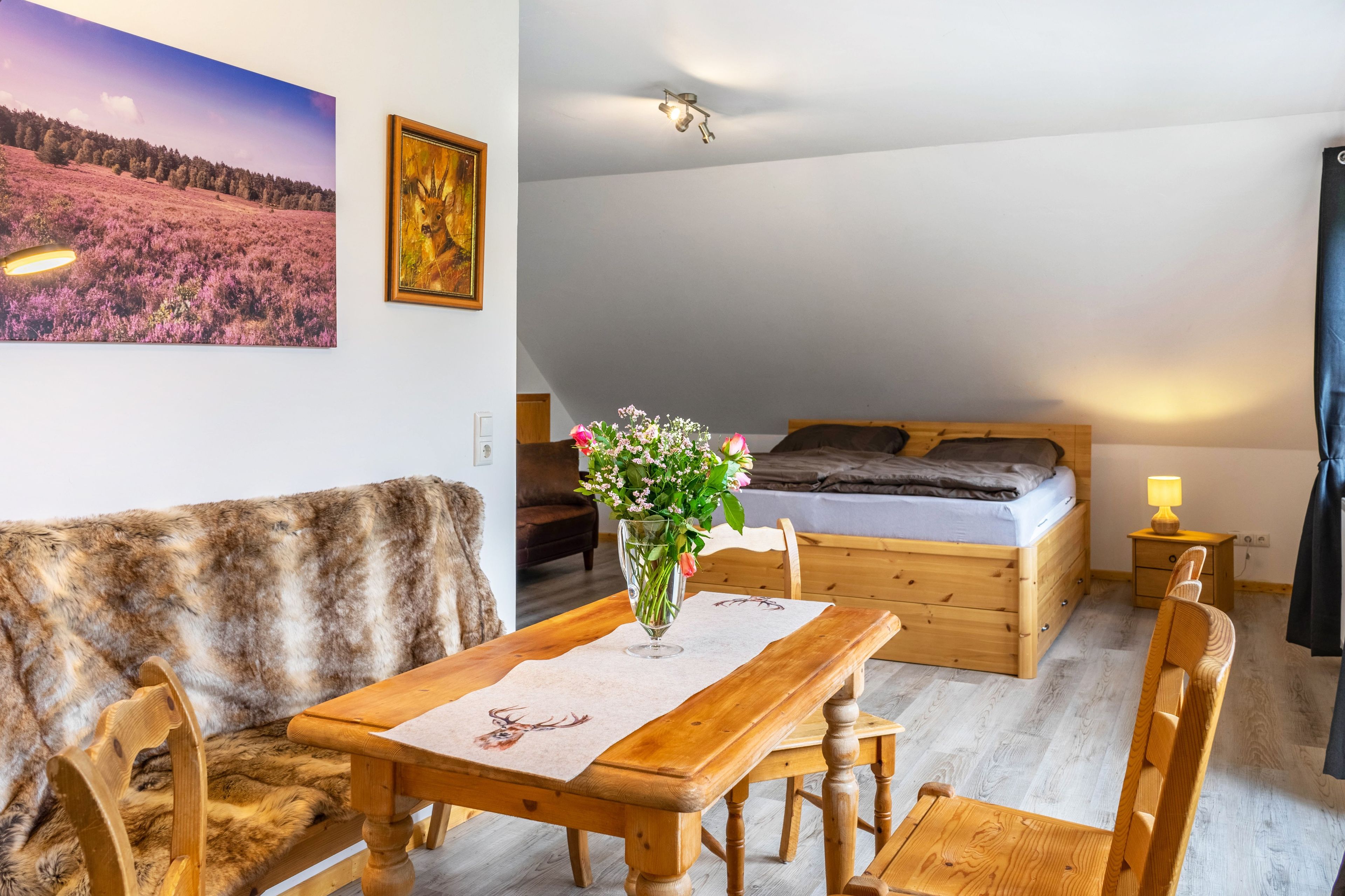 Ein gemütliches Zimmer mit einem Holztisch, einer Couch, einem Bett und einem Landschaftsbild.