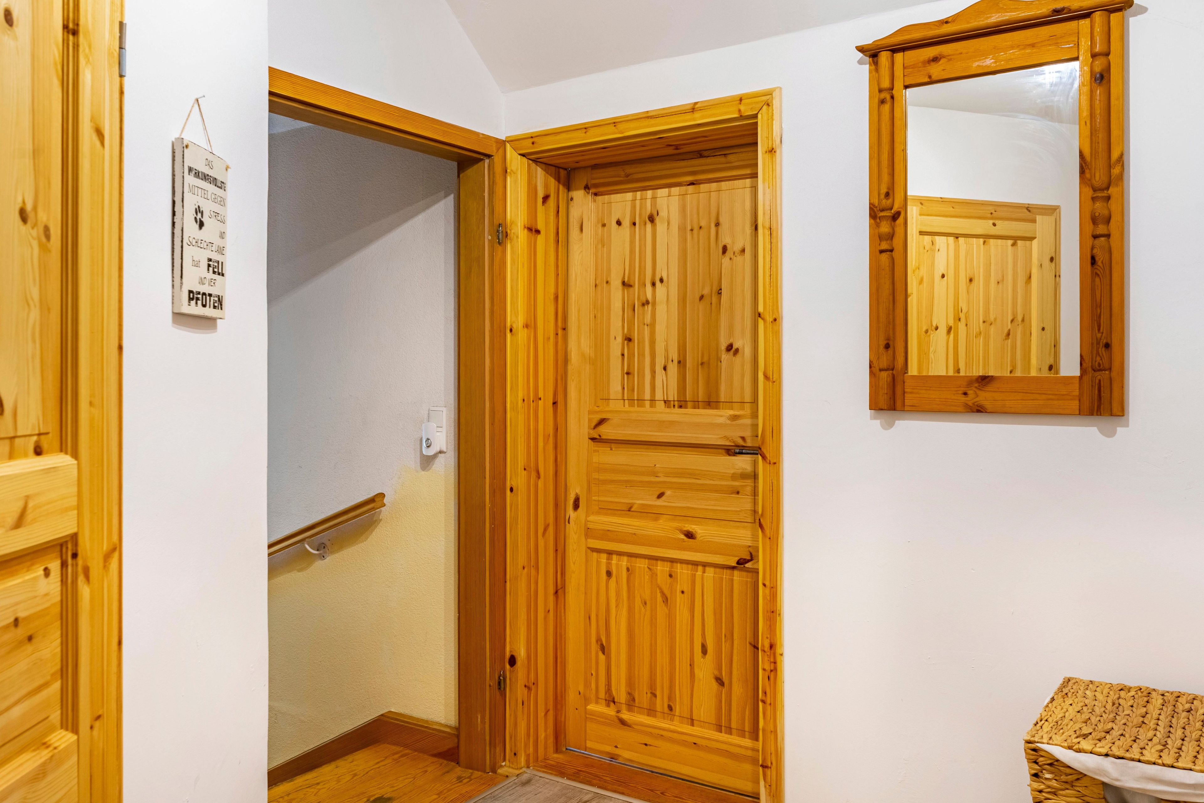 Eine Holztür mit einem Spiegel darüber, ein kleines Schild an der Wand und eine hölzerne Bank.