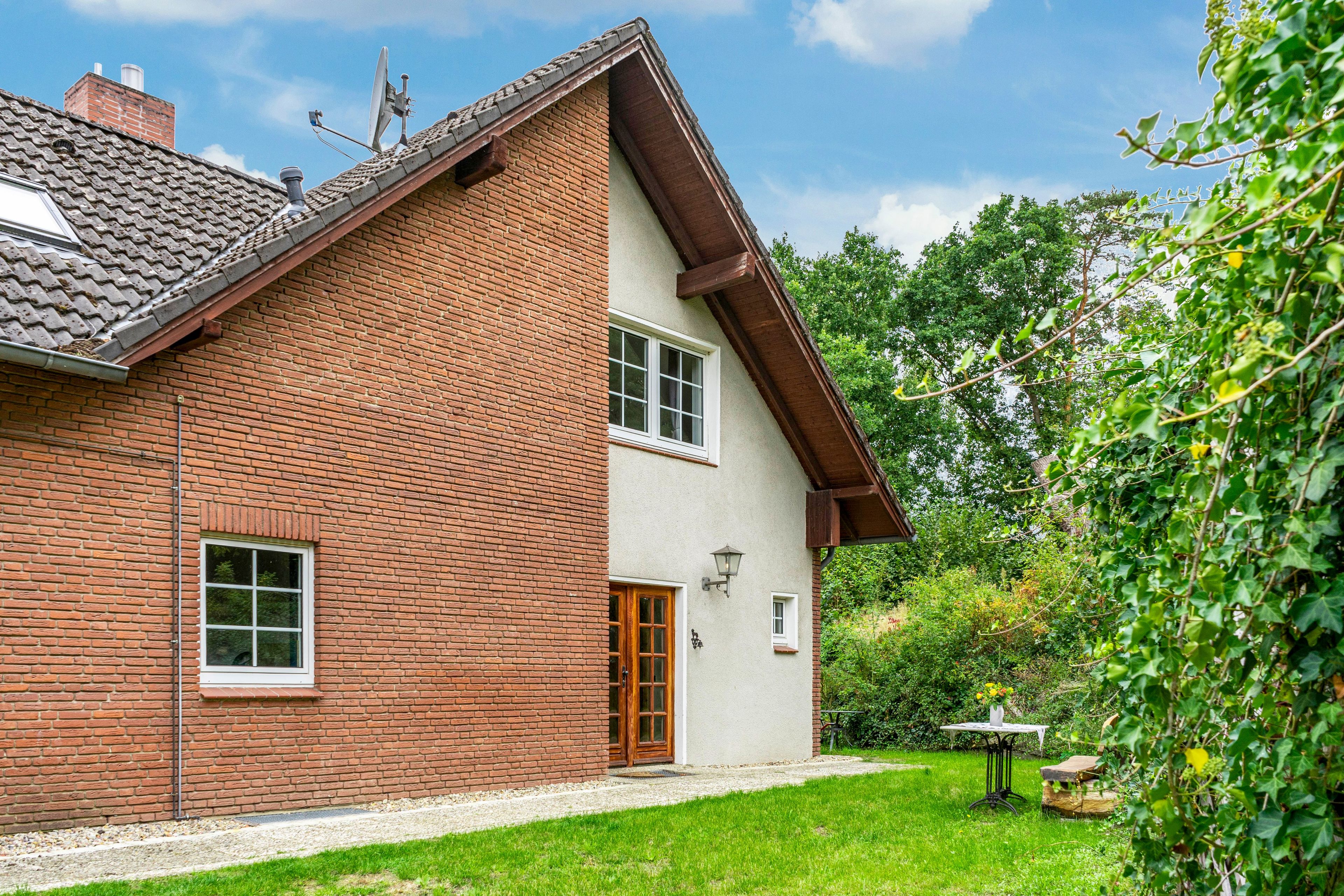 Ein zweistöckiges Haus mit Backsteinfassade, einem Ziegeldach und einem kleinen Garten mit Tisch und Stühlen.