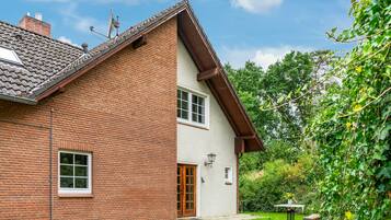 Ein zweistöckiges Haus mit Backsteinfassade, einem Ziegeldach und einem kleinen Garten mit Tisch und Stühlen.