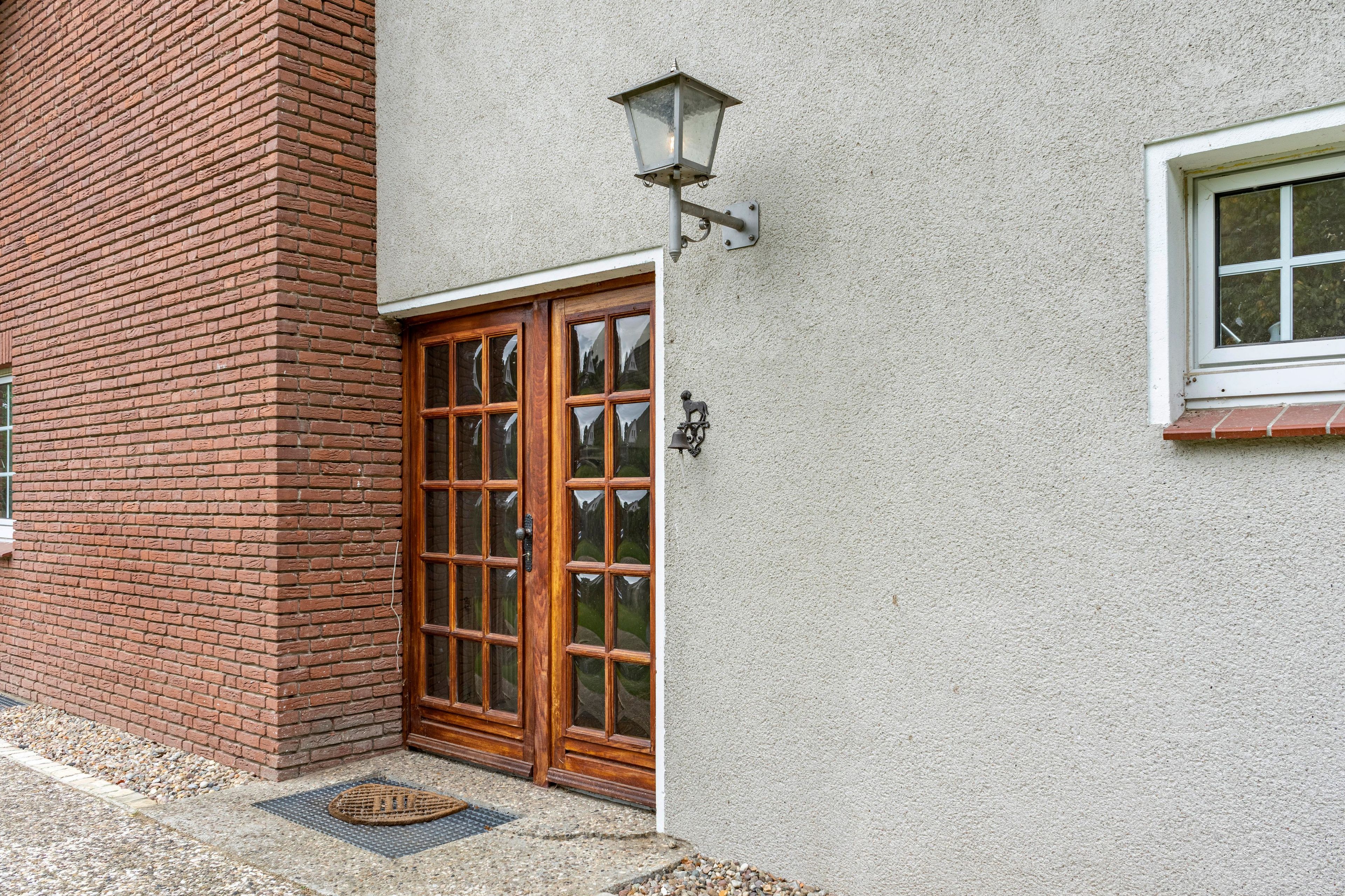 Ein Gebäude mit einer Ziegel-Fassade, einer zweiflügeligen Holztür mit Glasscheiben und einem kleinen Fenster mit weißem Rahmen.