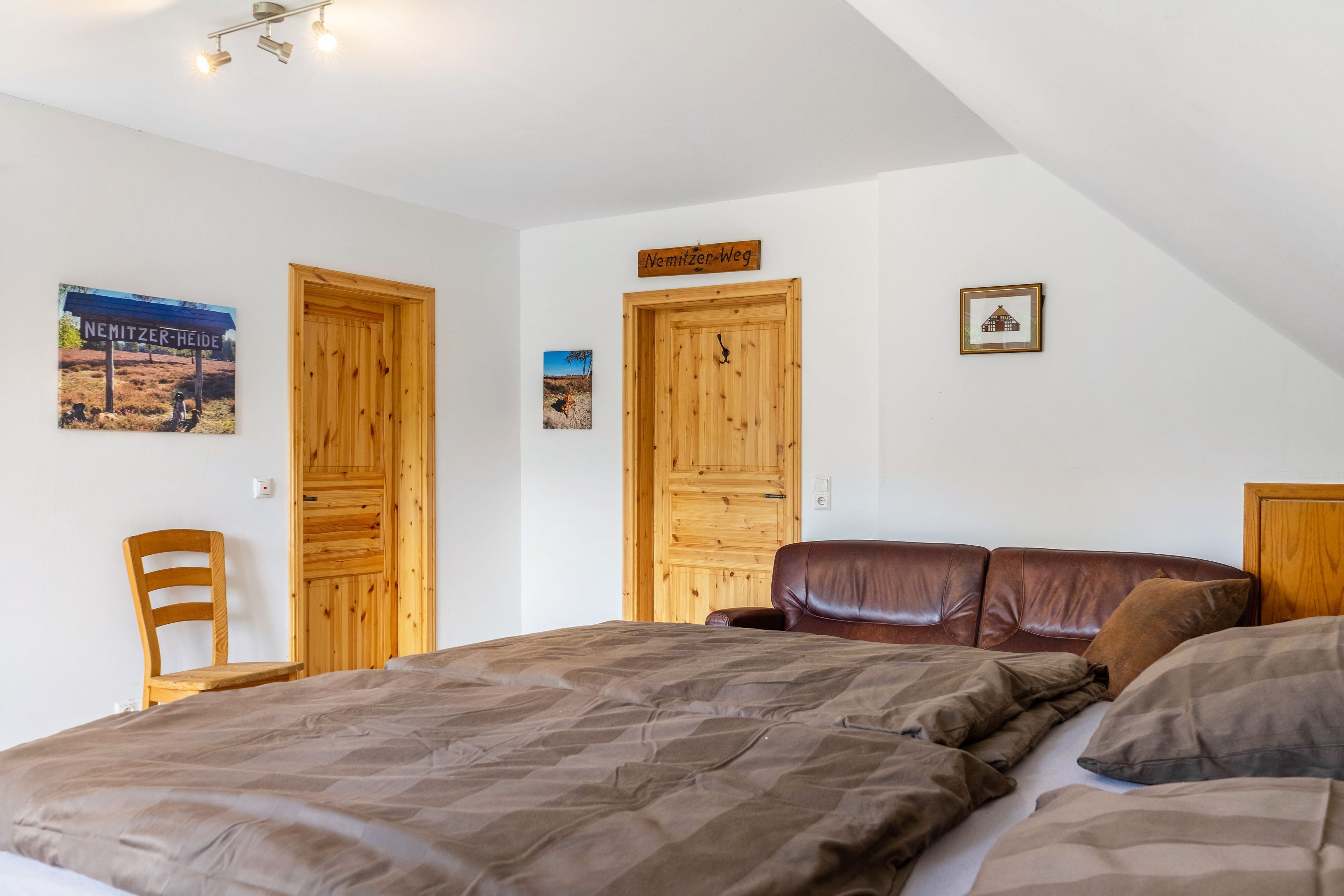 A bedroom with a large bed, wooden doors, a chair, and a small picture on the wall.