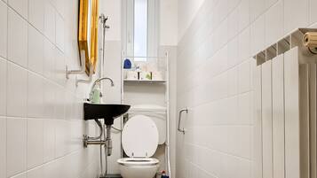 A narrow bathroom with white tiled walls, a wooden floor, a blue rug, a toilet, a sink, and a shower.