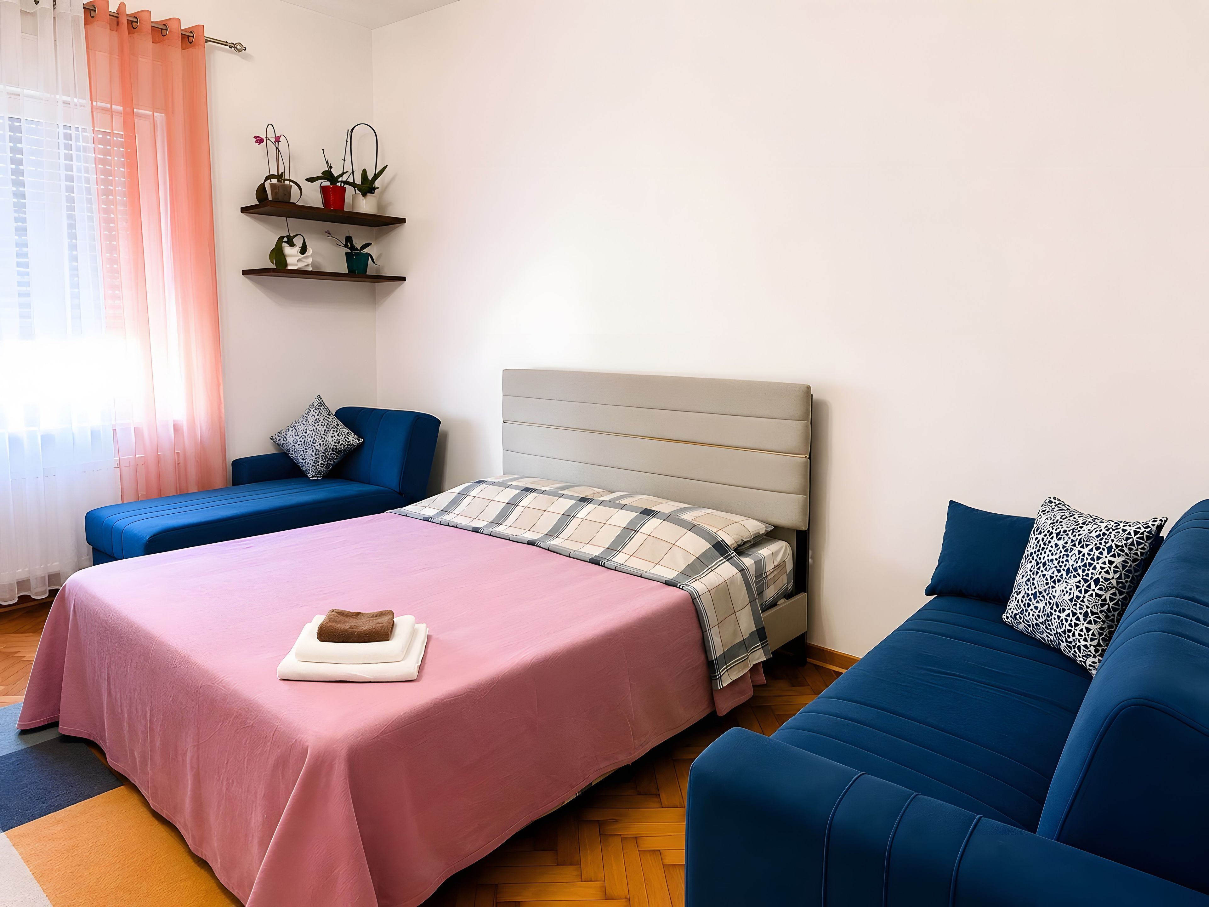 Une chambre à coucher avec un lit, deux canapés, une fenêtre avec des rideaux et une étagère avec des plantes.
