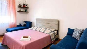 Une chambre à coucher avec un lit, deux canapés, une fenêtre avec des rideaux et une étagère avec des plantes.