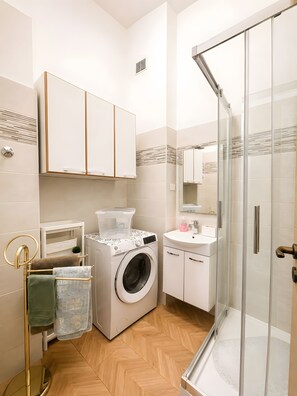 Ein modernes Badezimmer mit Waschmaschine, Waschbecken und einer Duschkabine aus Glas.