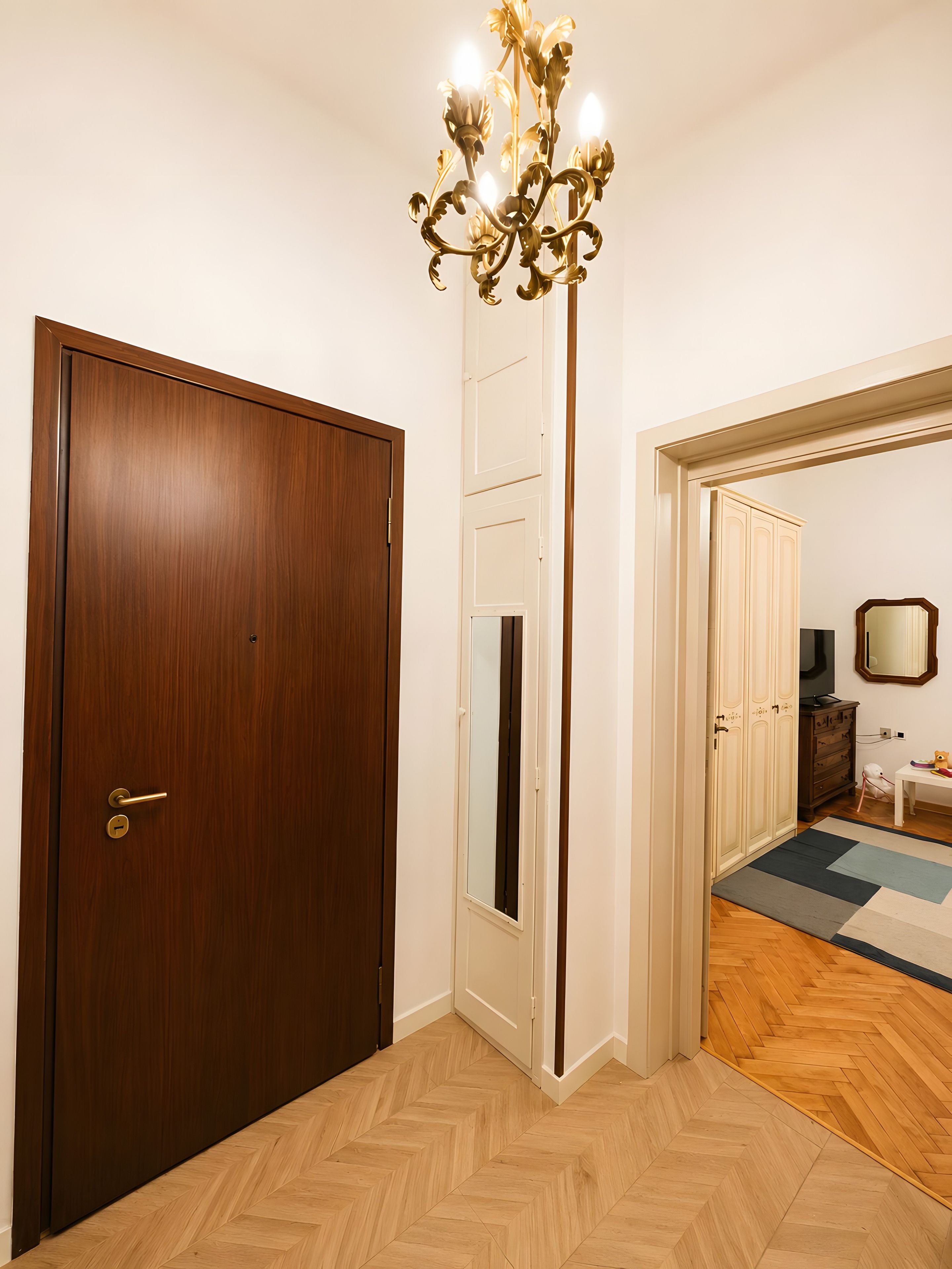 Ein Zimmer mit Holztür, weißer Wand, Spiegel, Kommode und einem Fischgrätparkettboden.