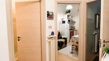 Un pasillo con suelo de madera, un equipo de aire acondicionado blanco y una puerta que da a una habitación con cama y planta.