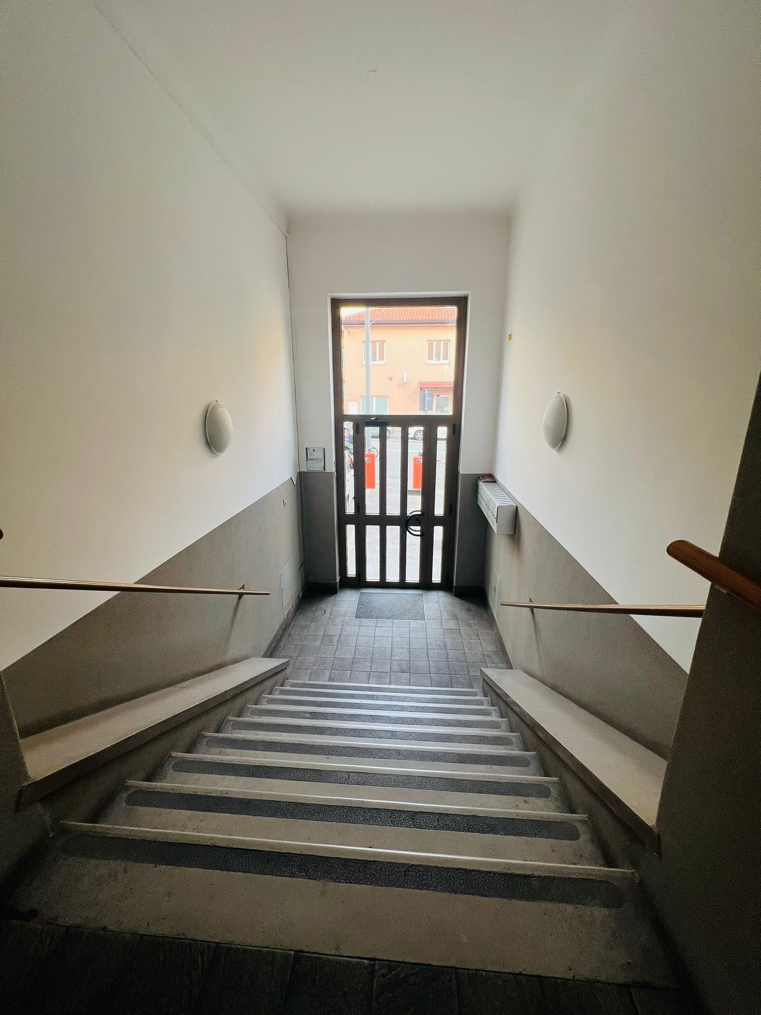 Eine Treppe führt zu einer Tür, durch die ein Blick auf ein Gebäude im Freien gewährt wird.