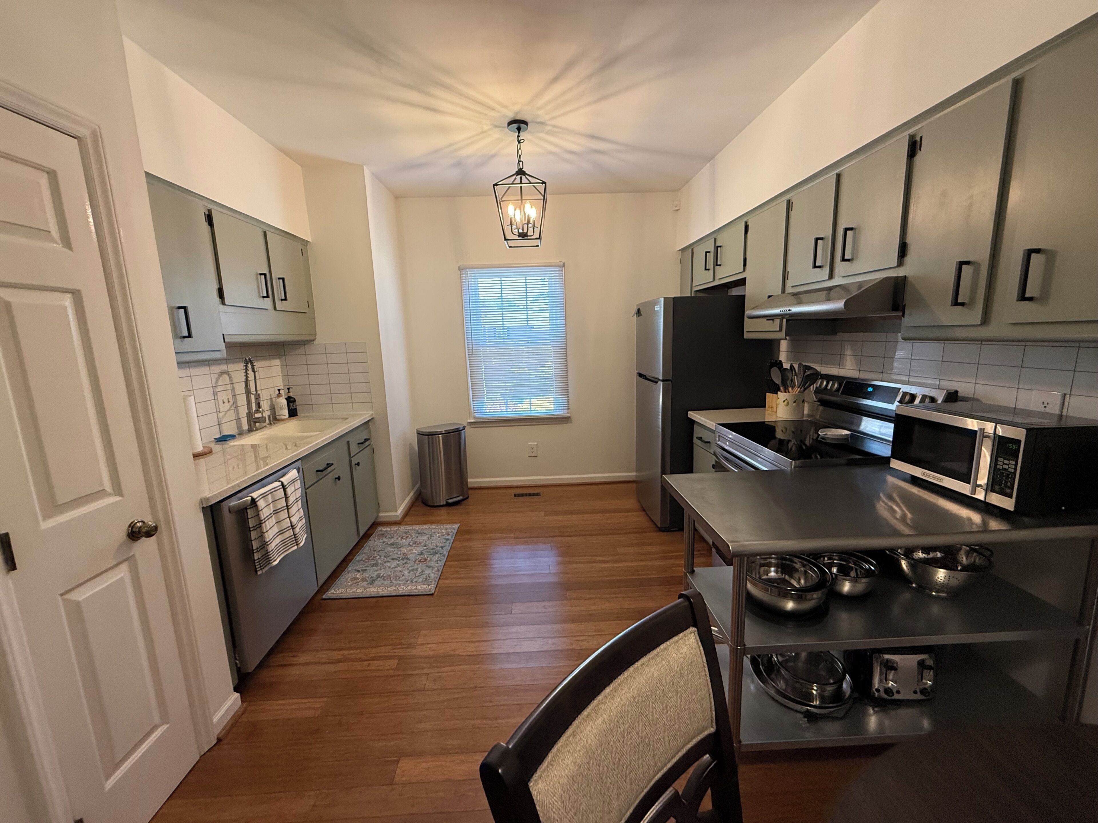 A modern kitchen with stainless steel appliances, a central island, and a window with blinds.