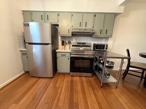 A compact kitchen with a stainless steel refrigerator, a built-in oven, a microwave, and light-colored cabinets. - Johnny’s Place: centrally located & fully loaded! (Raleigh)