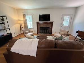 A living room with a fireplace, two armchairs, a sofa, and a television. - Johnny’s Place: centrally located & fully loaded! (Raleigh)