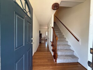 A hallway with a dark blue door, wooden stairs, and a carpeted floor. - Johnny’s Place: centrally located & fully loaded! (Raleigh)