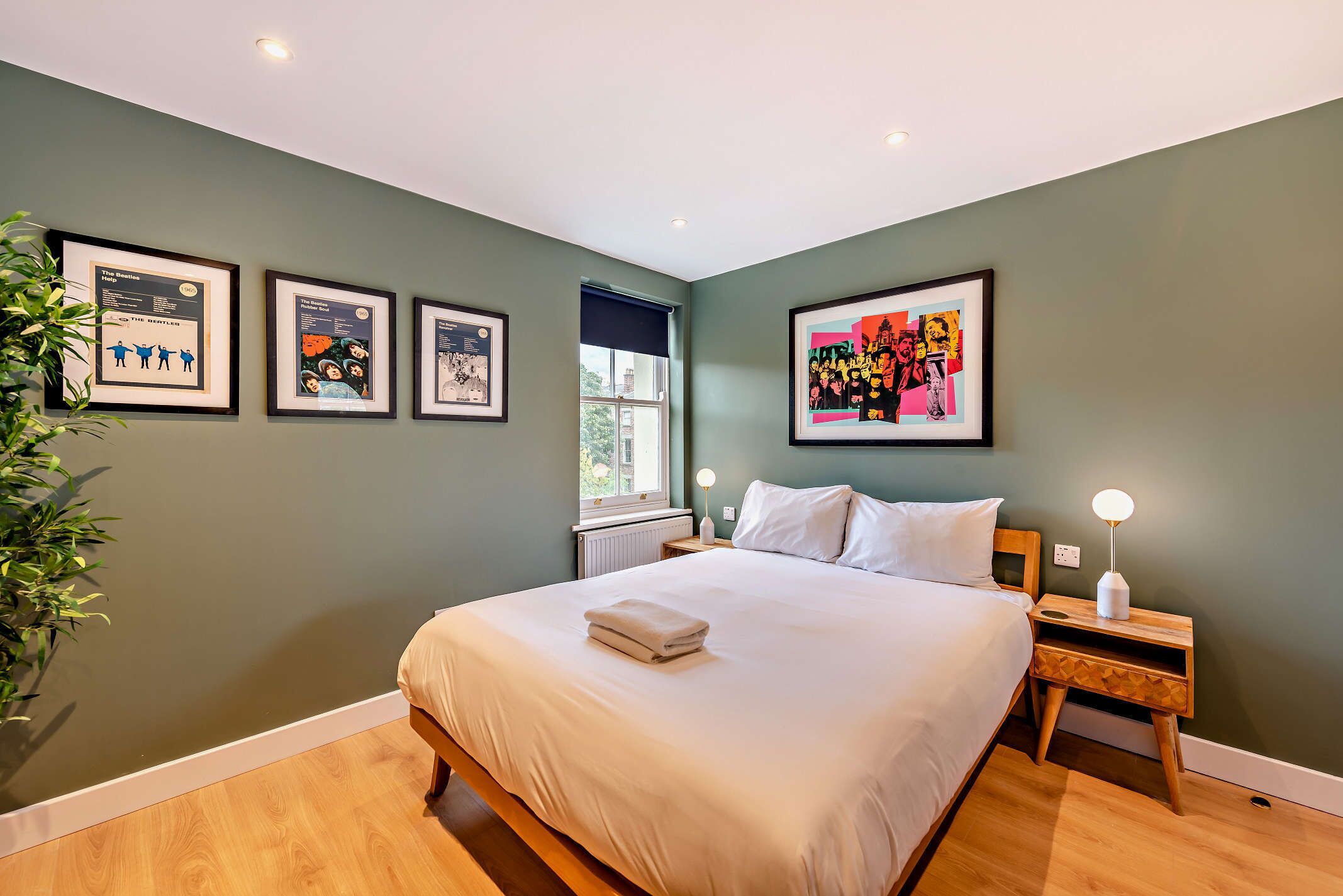 A bedroom with a bed, a nightstand, a lamp, and framed posters on the wall.