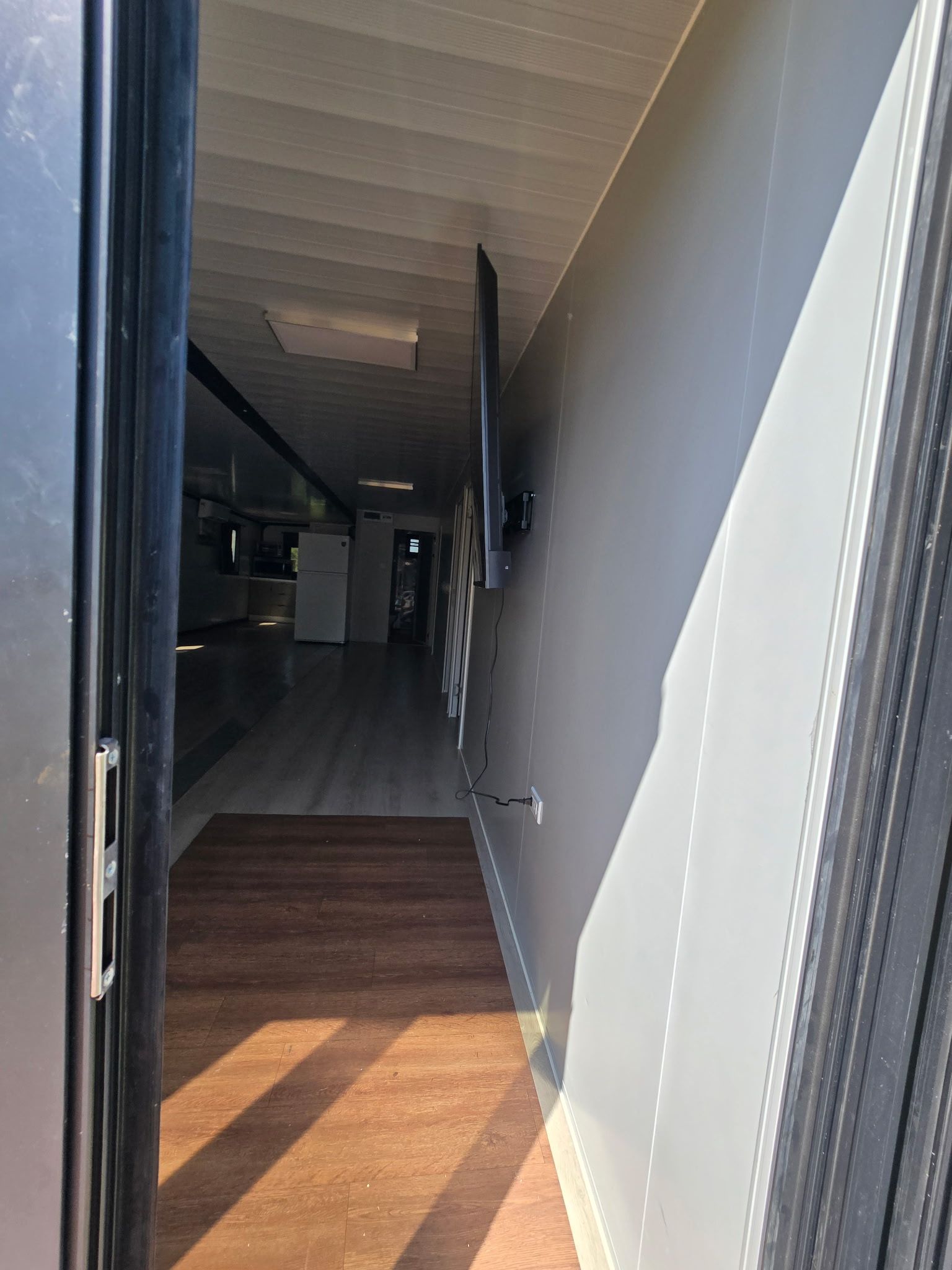 A hallway with a wooden floor leading to a kitchen area with appliances.