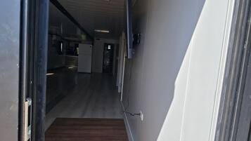 A hallway with a wooden floor leading to a kitchen area with appliances.
