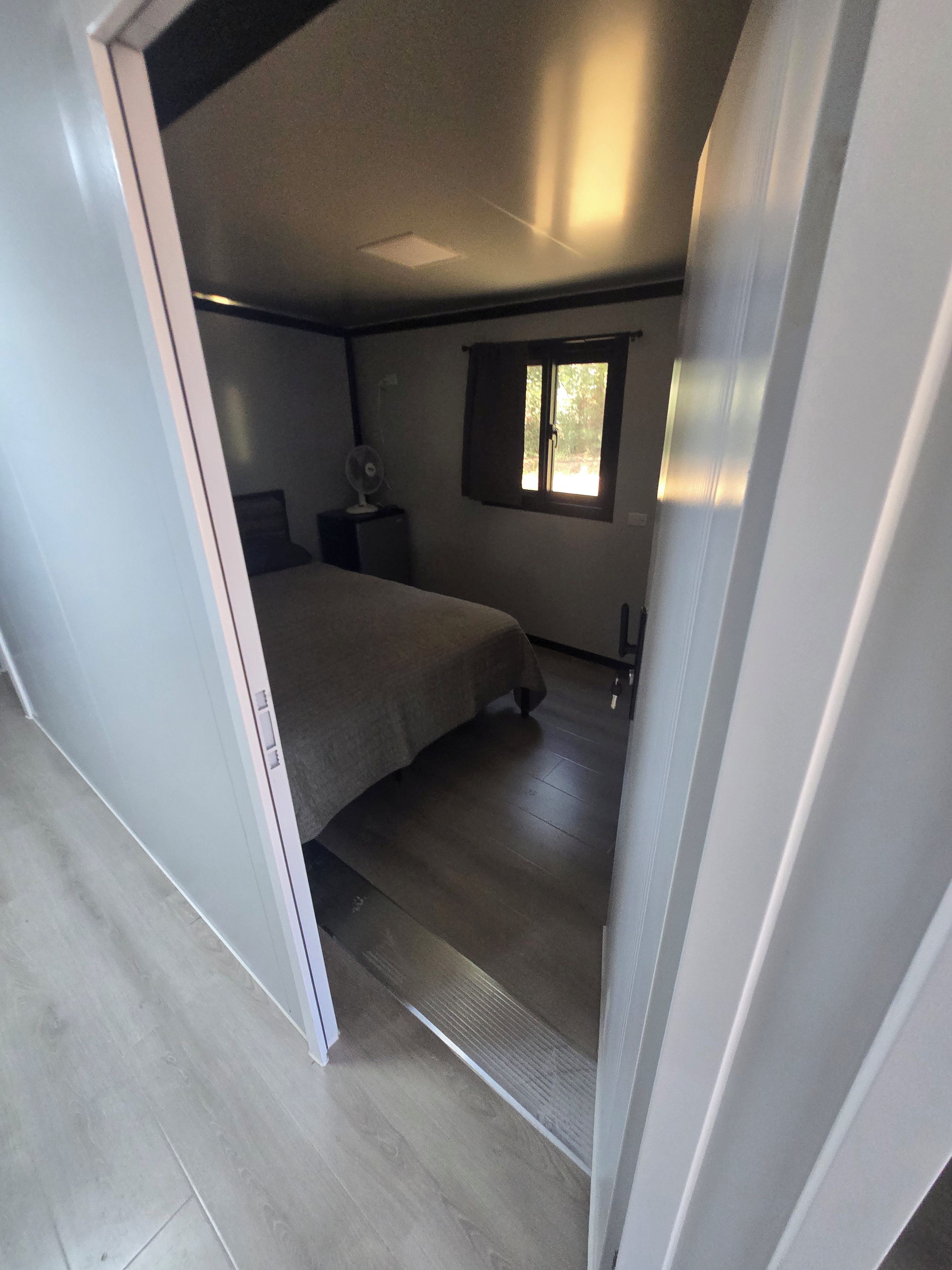 A compact bedroom with a bed, a bedside table, a window, and a fan.