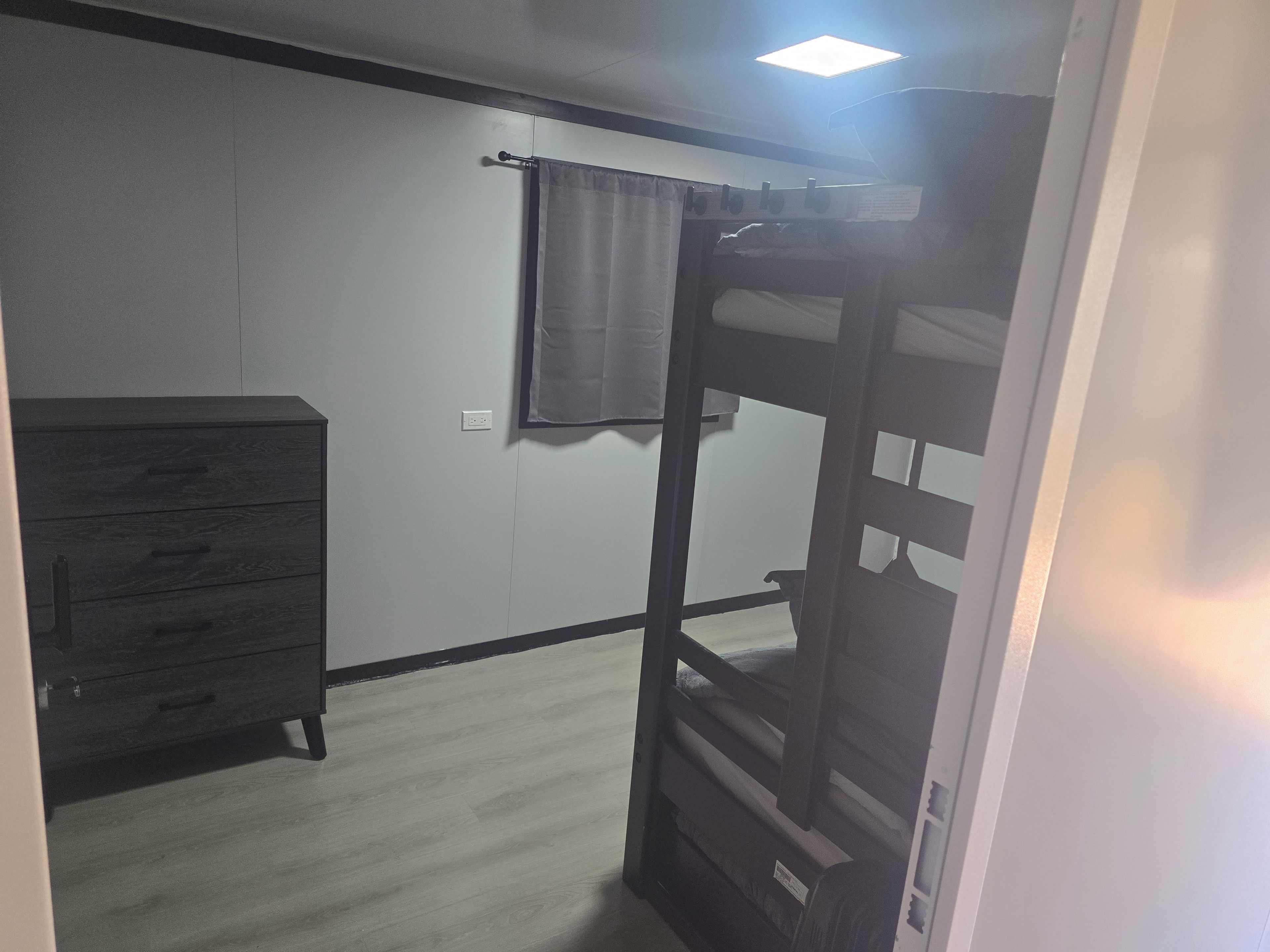 Une chambre avec un lit superposé, une commode et un interrupteur sur le mur.