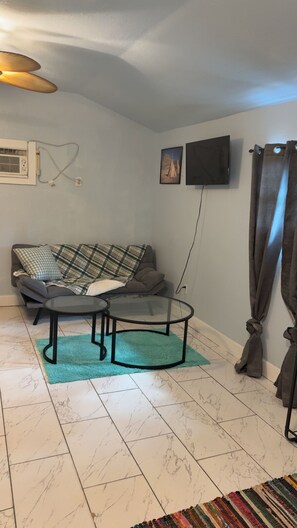 A living room with a sofa, a glass coffee table, a flat-screen TV, and a wall-mounted air conditioning unit. - Private Sarasota Guest House Near Beaches, Downtown & Siesta Key (Sarasota)