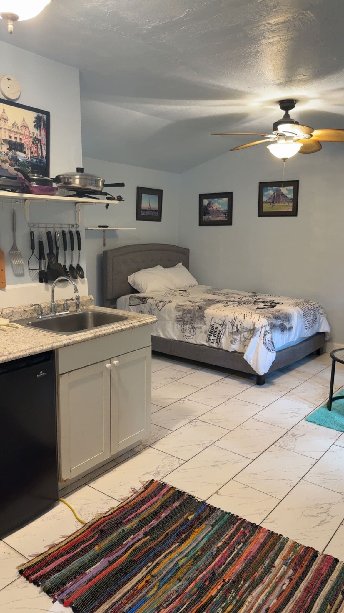 A compact bedroom with a bed, a nightstand, a ceiling fan, and a small window.