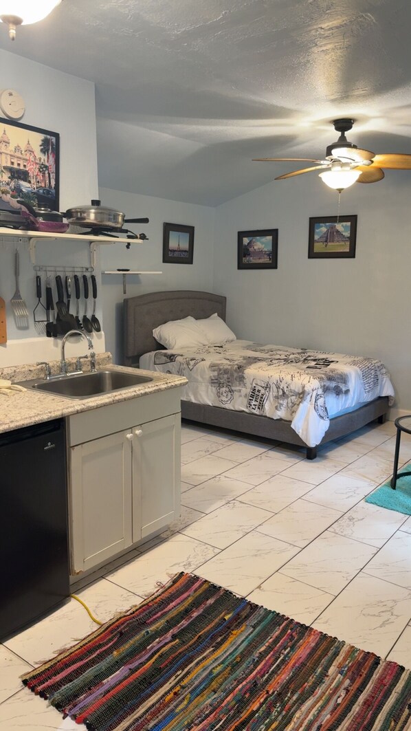 A compact bedroom with a bed, a nightstand, a ceiling fan, and a small window.