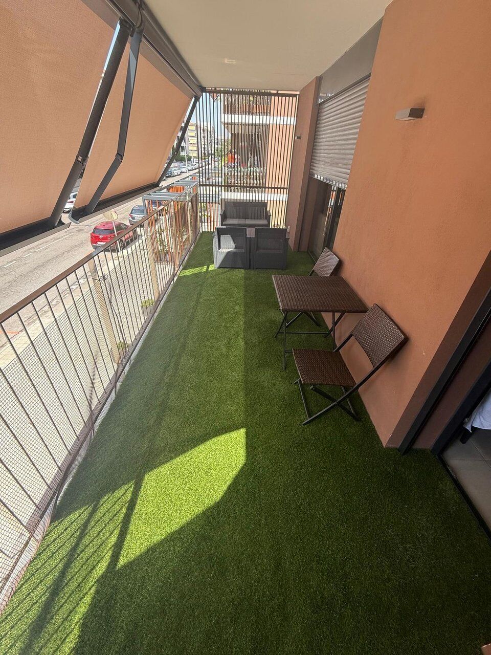 Un balcón con césped artificial, dos sillas plegables y una mesa.