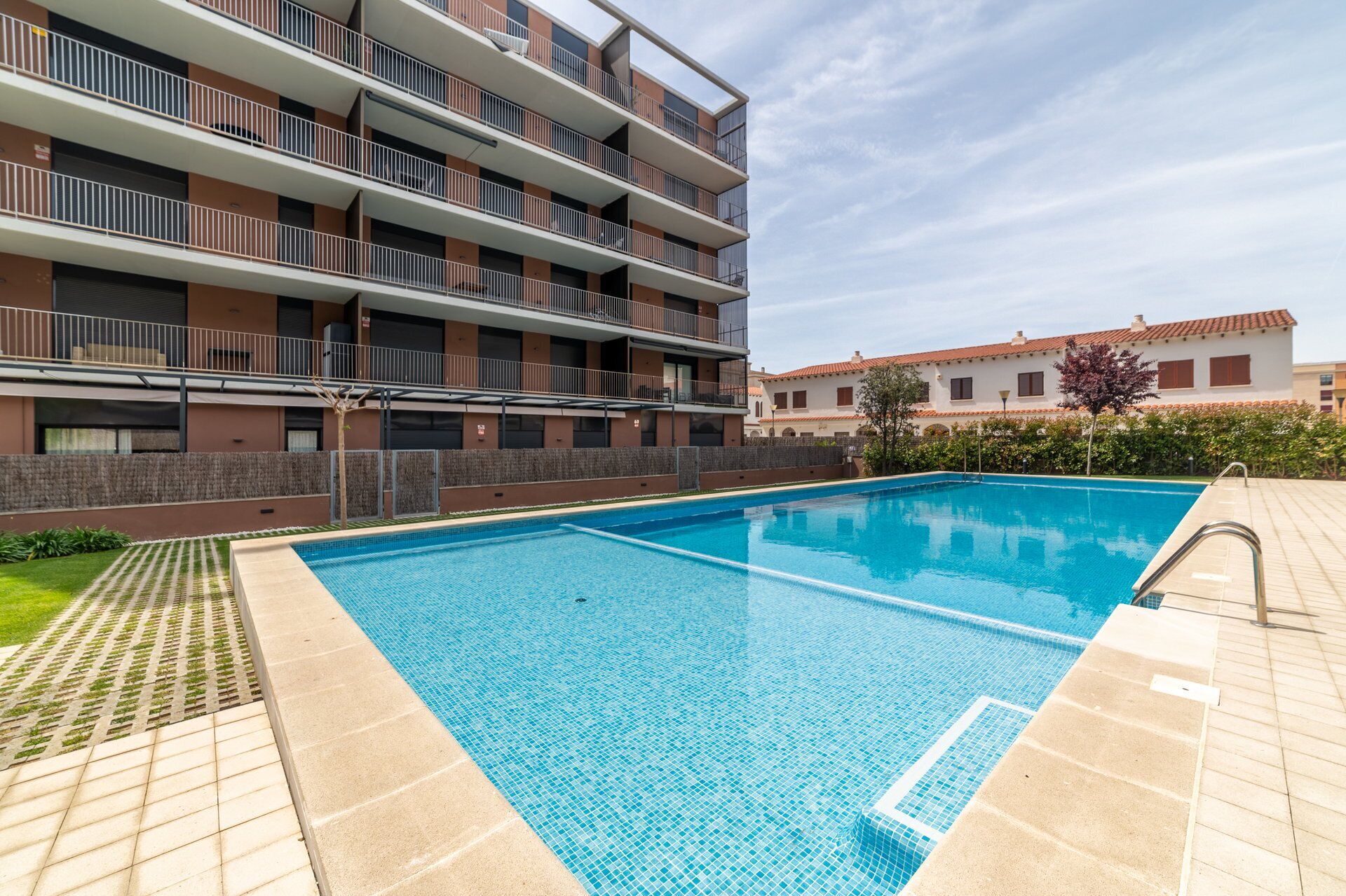 A modern apartment building with a swimming pool, balconies, and a clear sky.