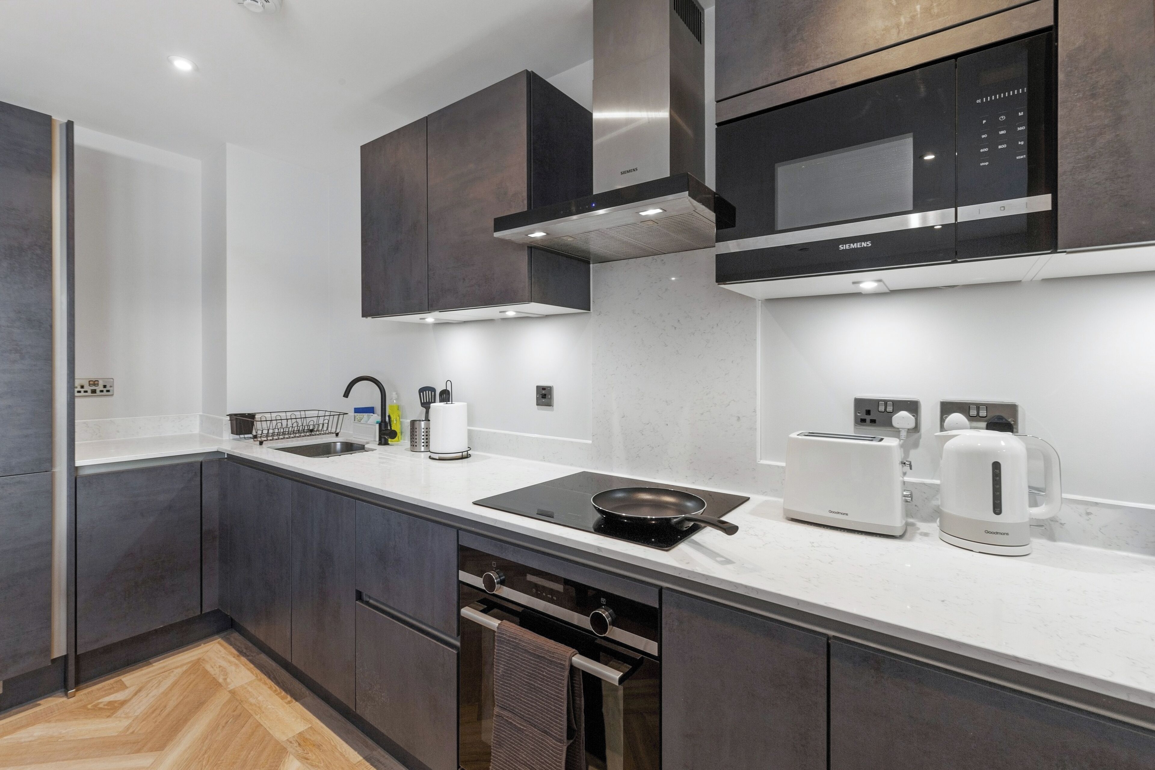 A modern kitchen with dark cabinetry, a stainless steel range hood, a microwave, a toaster, and a kettle.